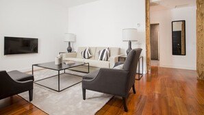 Een moderne woonkamer met een bank, twee fauteuils, een salontafel en een televisie.
