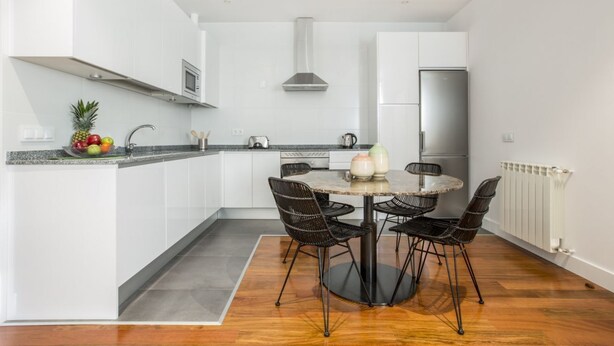 Een moderne keuken met witte kastjes, een roestvrijstalen koelkast, een magnetron en een ronde eettafel met vier zwarte stoelen.
