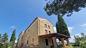 Un edificio de piedra con un porche cubierto, rodeado de árboles y grava.
