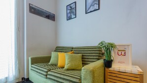 Ein grünes Sofa mit gestreiften Kissen, ein kleiner Holztisch mit einem Blumentopf und gerahmte Bilder an der Wand.