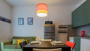 En kompakt opholdsstue med spisebord, stole, sofa og et tekøkken med køleskab og skabe.