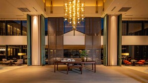 A spacious lobby with a modern chandelier, a seating area with tables and chairs, and a decorative wall with intricate patterns. - Nanhu Hotel (Jiaxing)