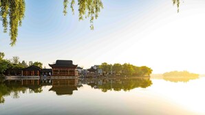 A traditional Chinese pavilion by a calm lake with clear reflections, surrounded by lush greenery and traditional architecture. - Nanhu Hotel (Jiaxing)