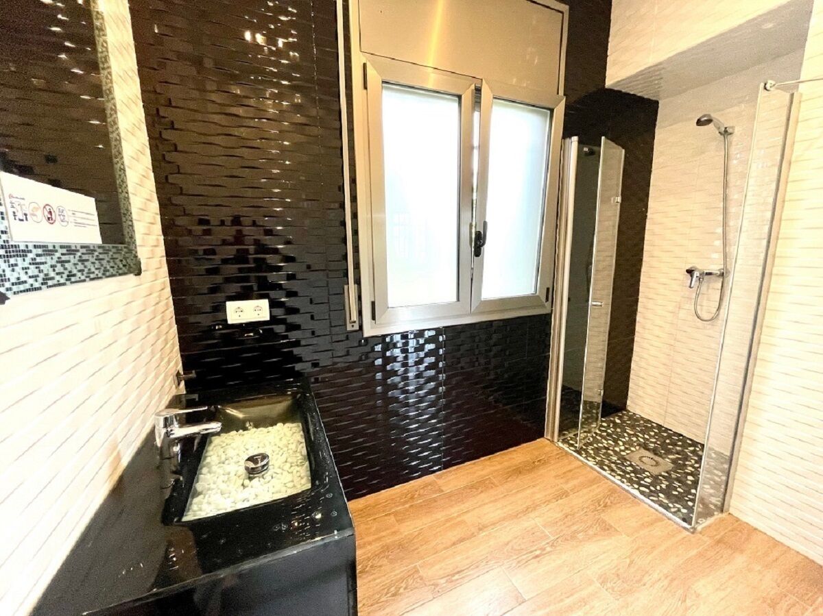 Une salle de bain moderne avec un mur recouvert de carreaux noirs, un lavabo doté d’un plan de toilette noir et un espace douche avec une porte en verre.