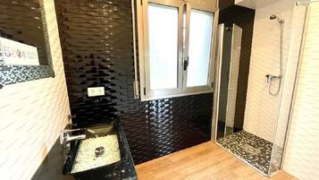 Une salle de bain moderne avec un mur recouvert de carreaux noirs, un lavabo doté d’un plan de toilette noir et un espace douche avec une porte en verre.