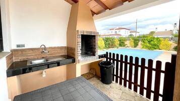 Une cuisine extérieure équipée d’un évier, d’un barbecue et offrant une vue sur une piscine.