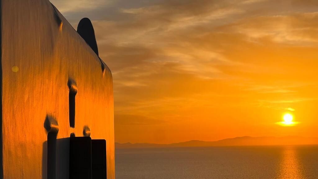 A sunset over a body of water with a building silhouette.