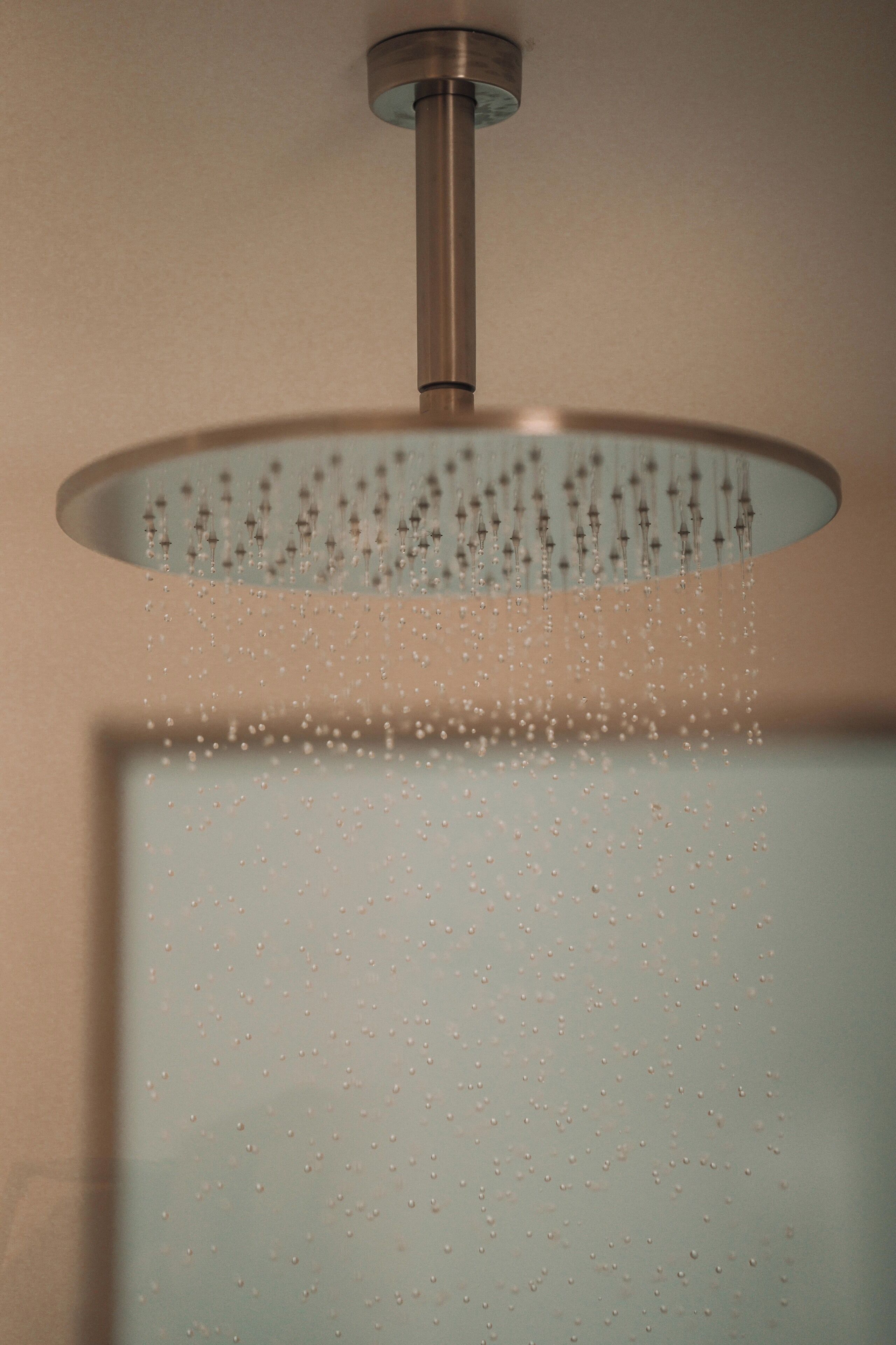 A ceiling-mounted shower with a circular design and water droplets visible.