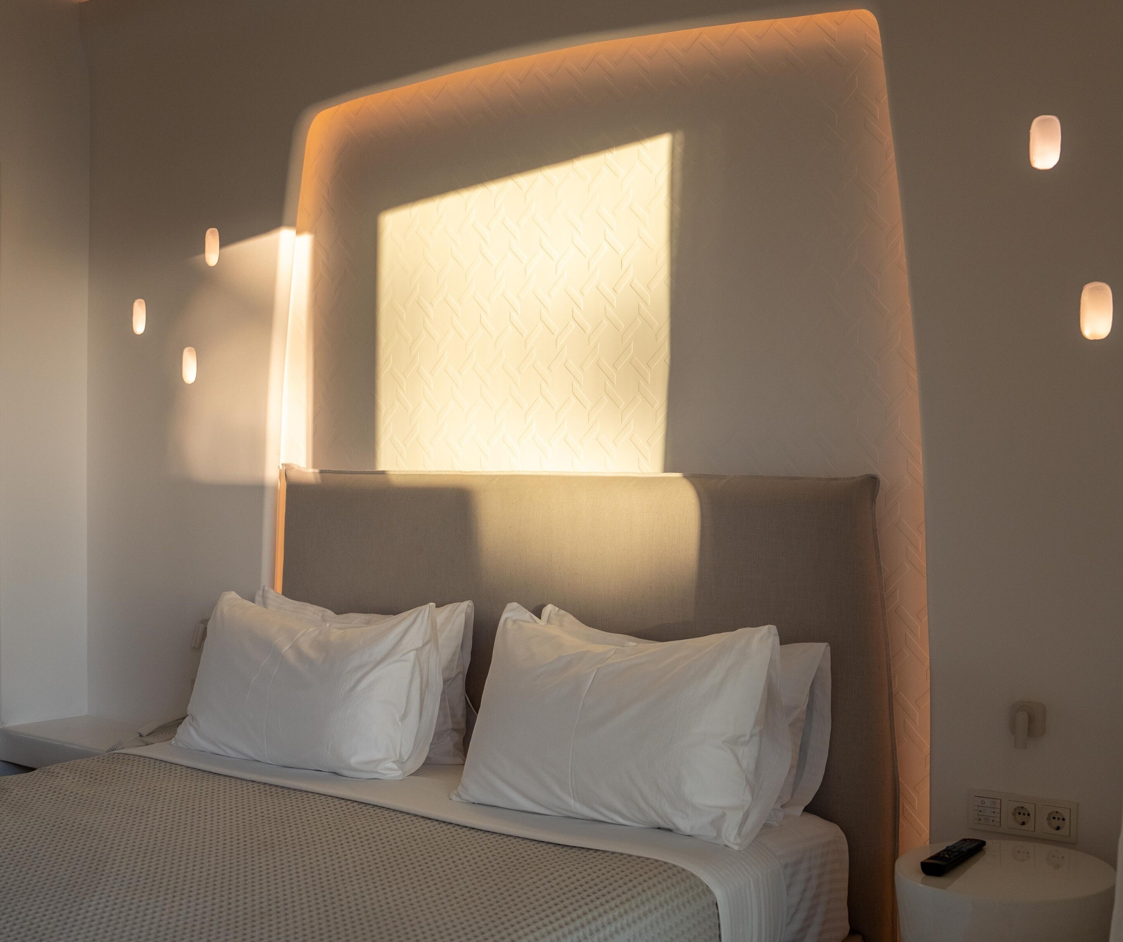 A modern hotel room with a large bed, a headboard with built-in lighting, and a small bedside table with a remote control.