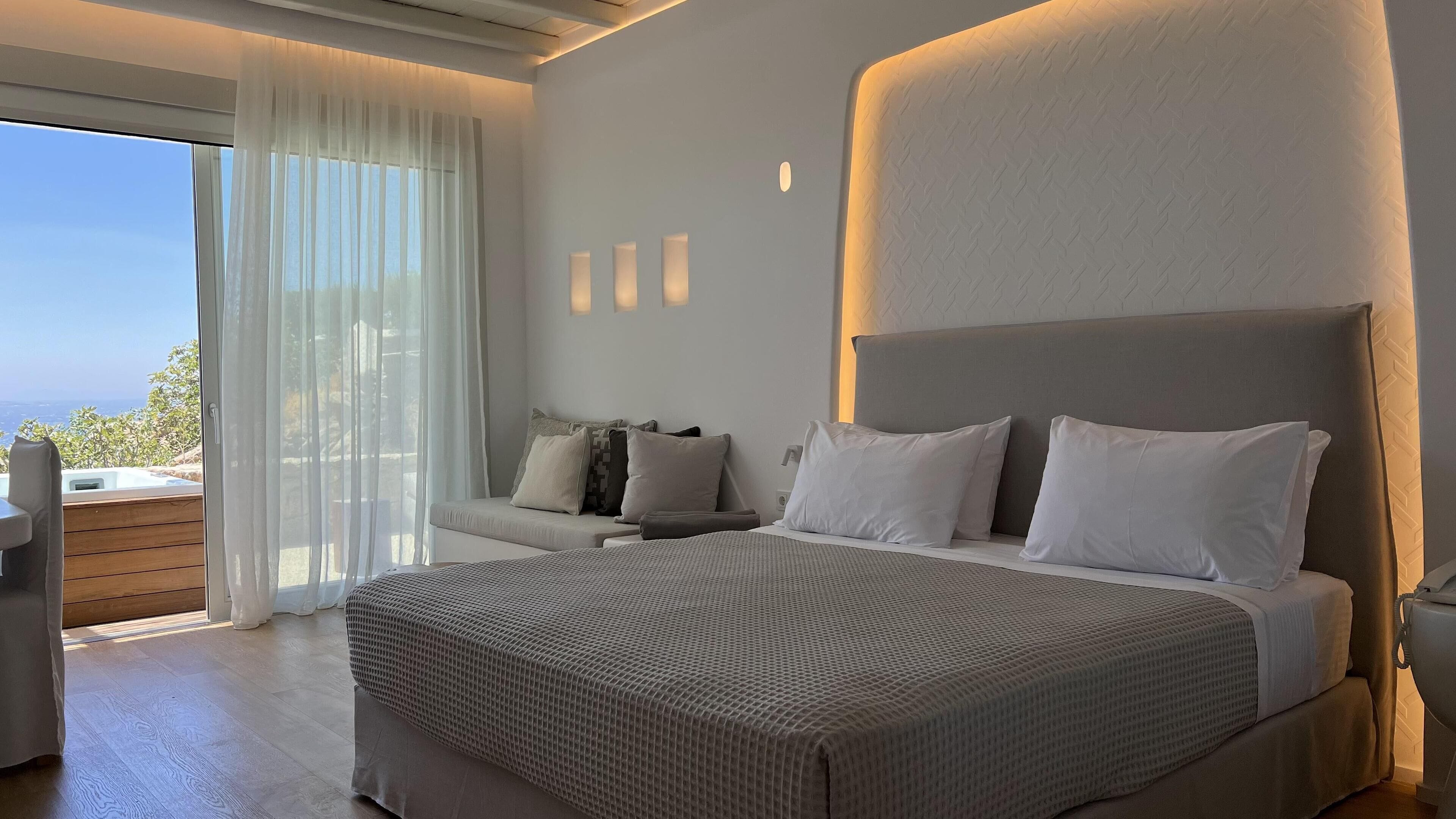 A modern bedroom with a large bed, a sofa, and a view of the outdoors.