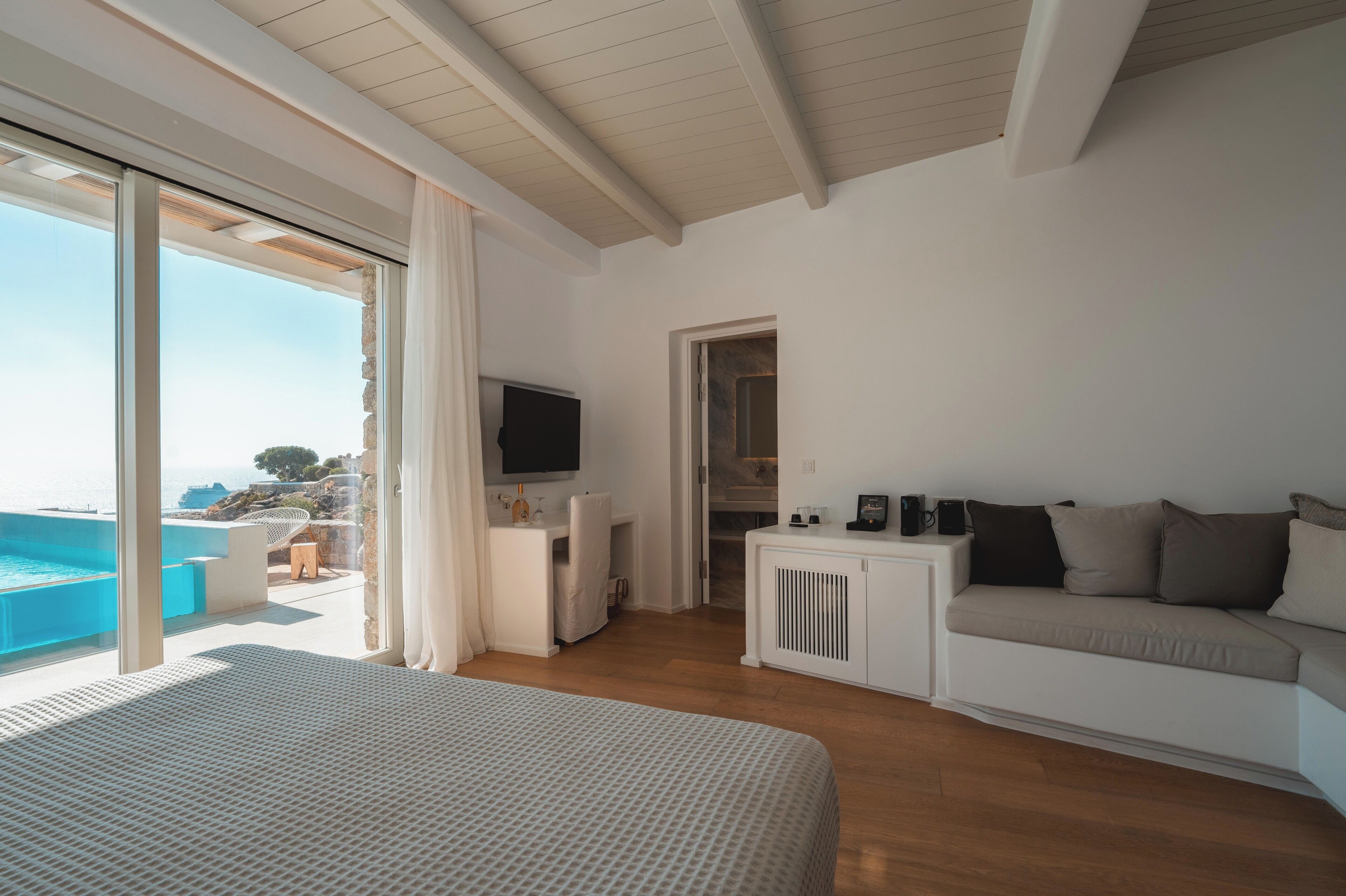 Ein modernes Hotelzimmer mit einem großen Bett, einer Couch, einem Fernseher und Meerblick.