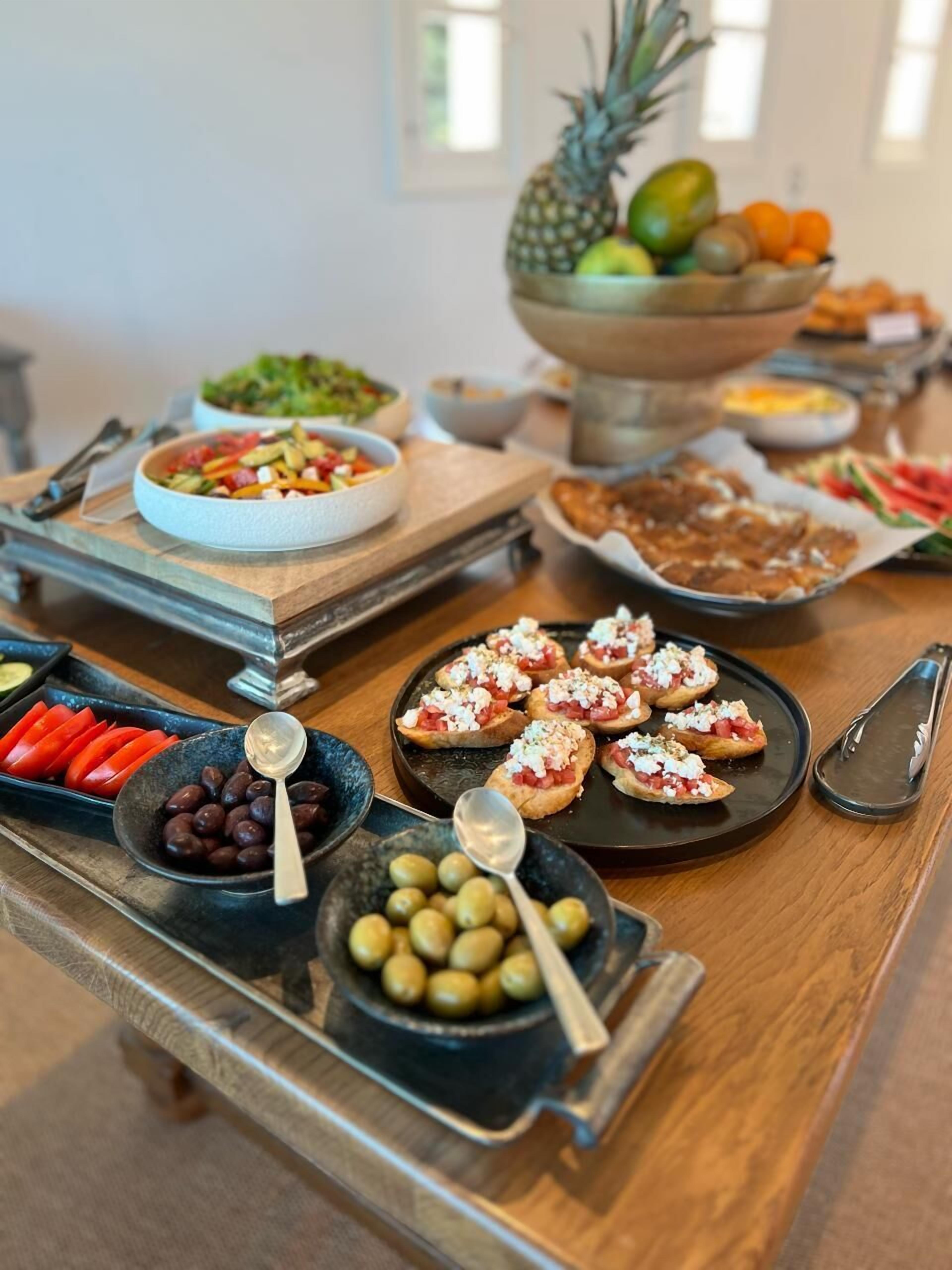 A buffet table with various food items including olives, tomatoes, and a pineapple.