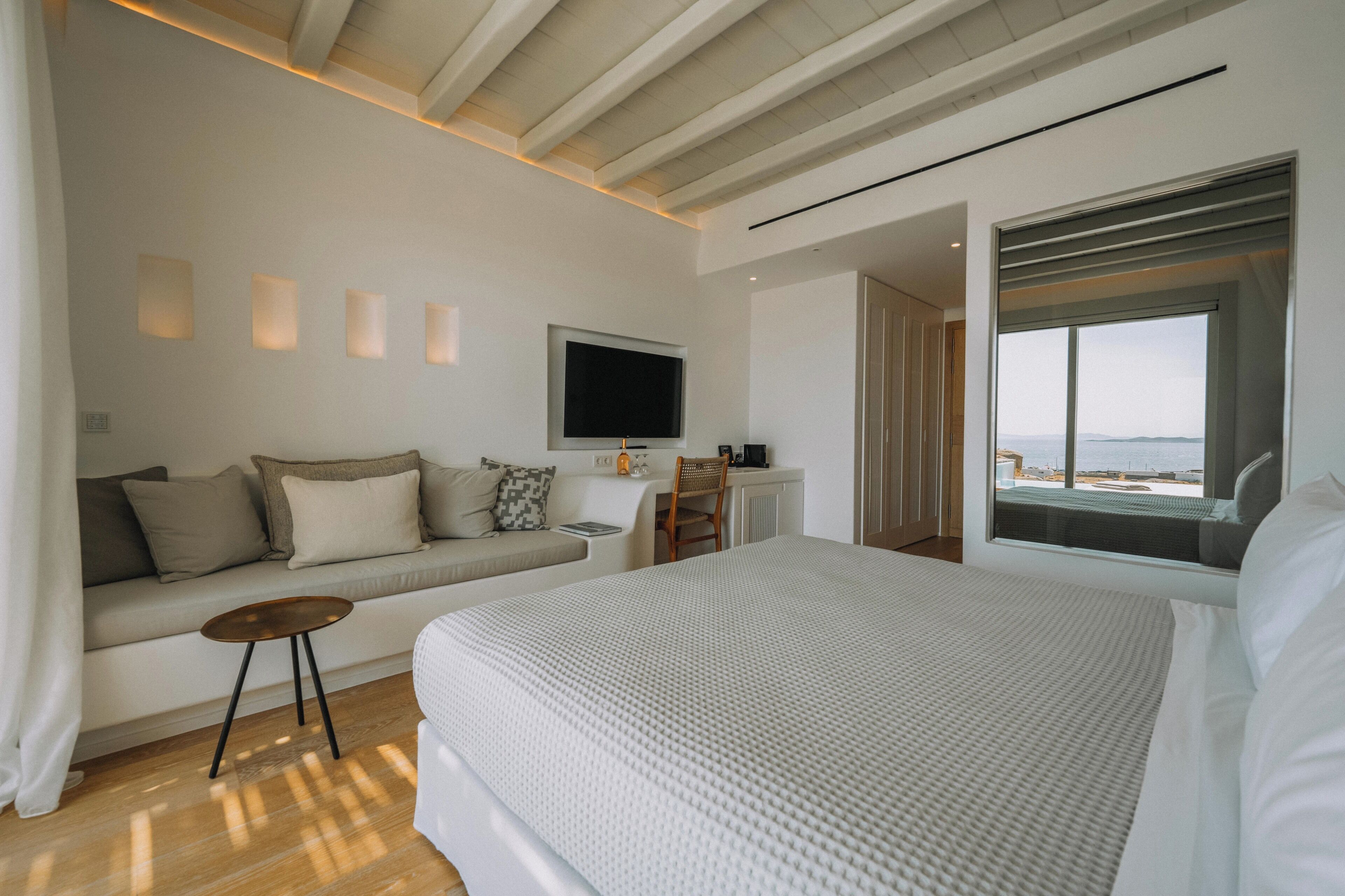 A modern hotel room with a large bed, a sofa, a TV, and a window with a view.