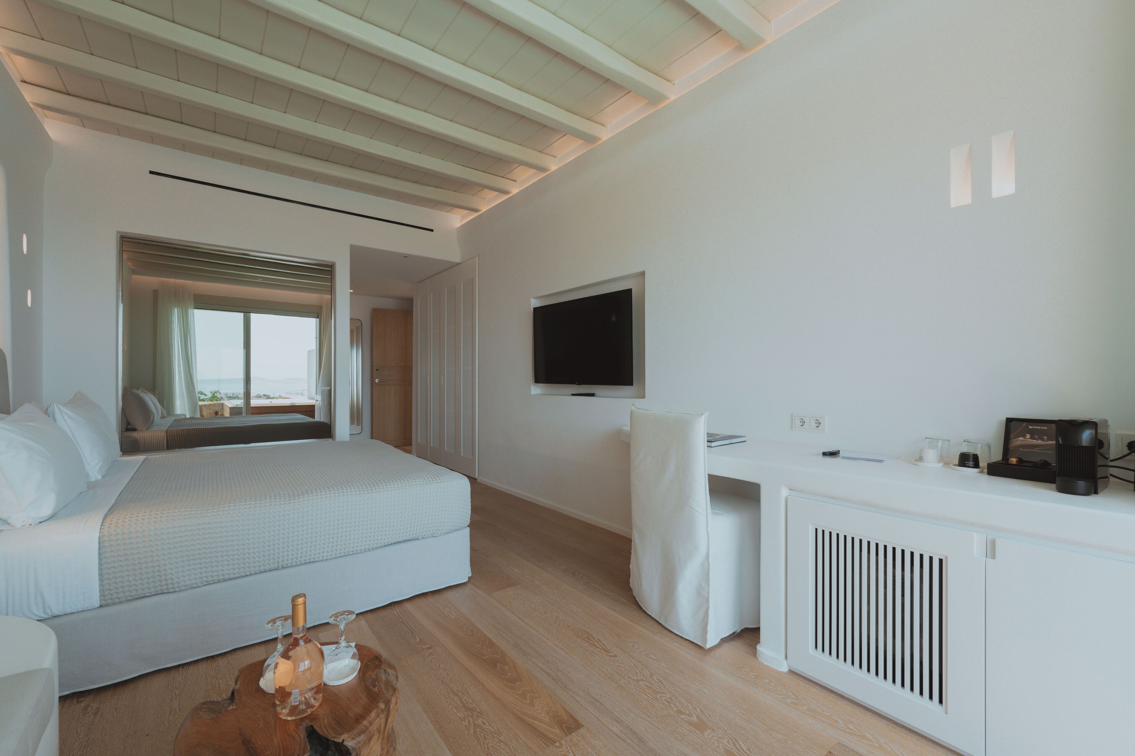 A modern hotel room with a bed, a desk, a television, and a view of the beach.
