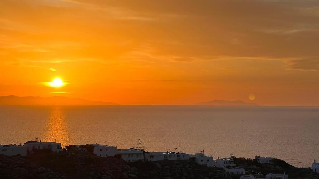 Vista de un atardecer costero con edificios en una colina.