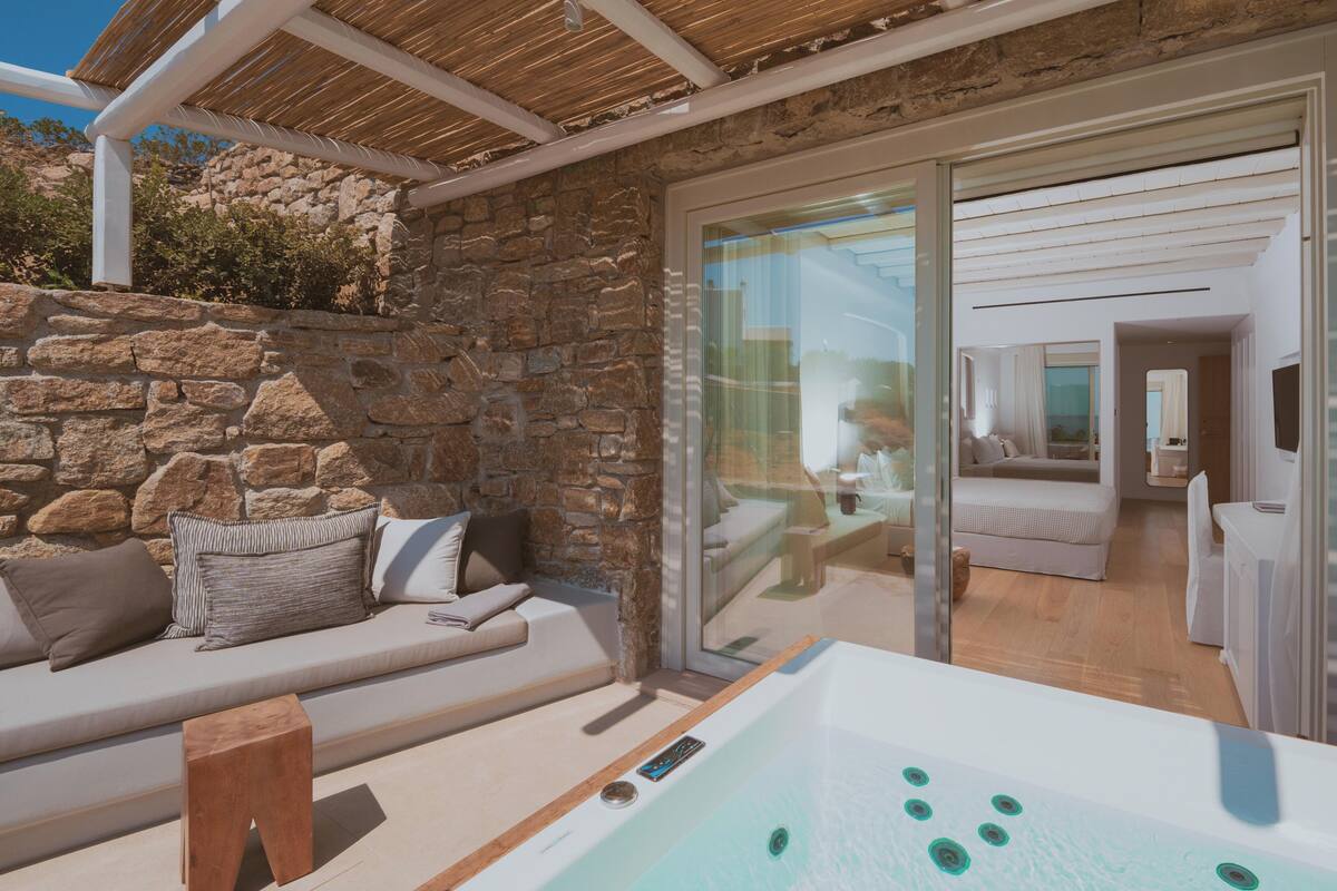 Un espace de vie extérieur moderne, agrémenté d’un mur en pierre, d’une porte vitrée donnant sur une pièce et d’un jacuzzi.