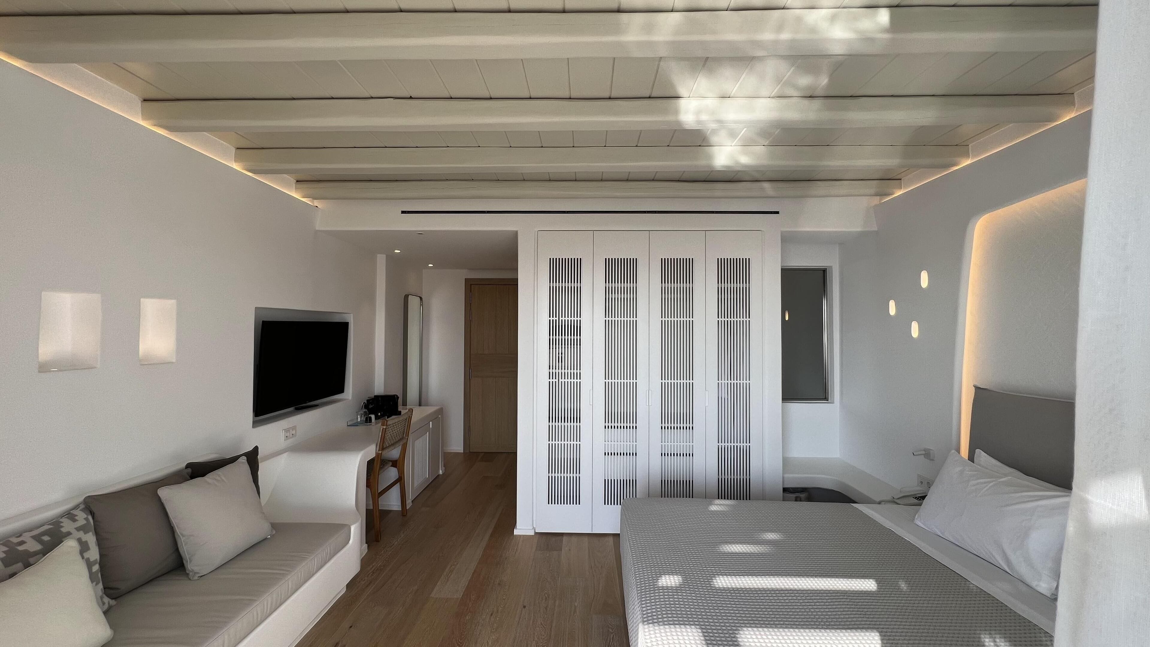 A modern hotel room with a bed, a sofa, a TV, and a sliding door.