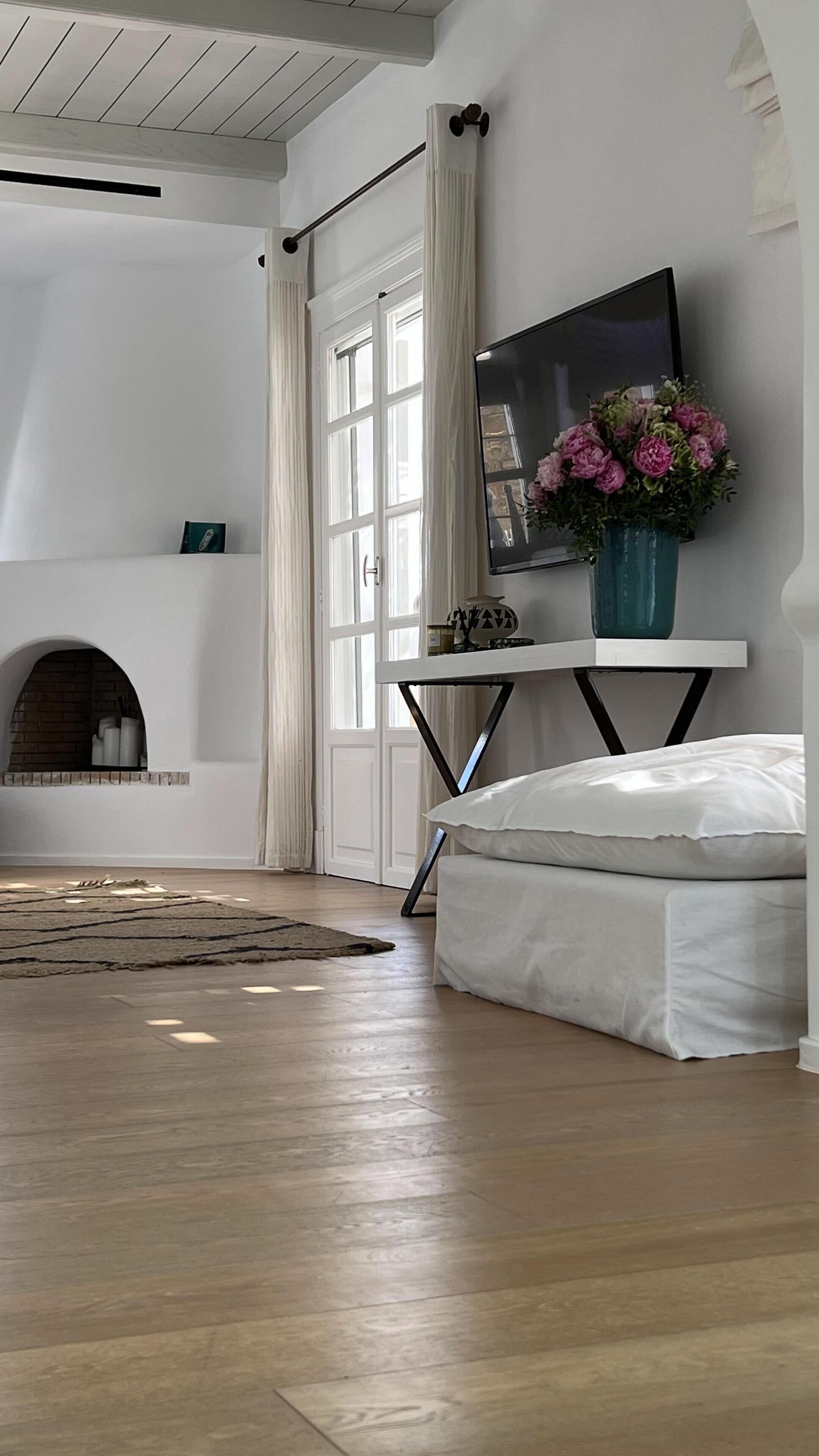 Een slaapkamer met een groot raam, een open haard, een bed, een televisie en een bloemenvaas.