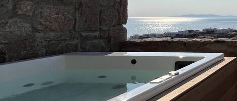 Muro de piedra con terraza de madera y bañera de hidromasaje con vista a un cuerpo de agua.