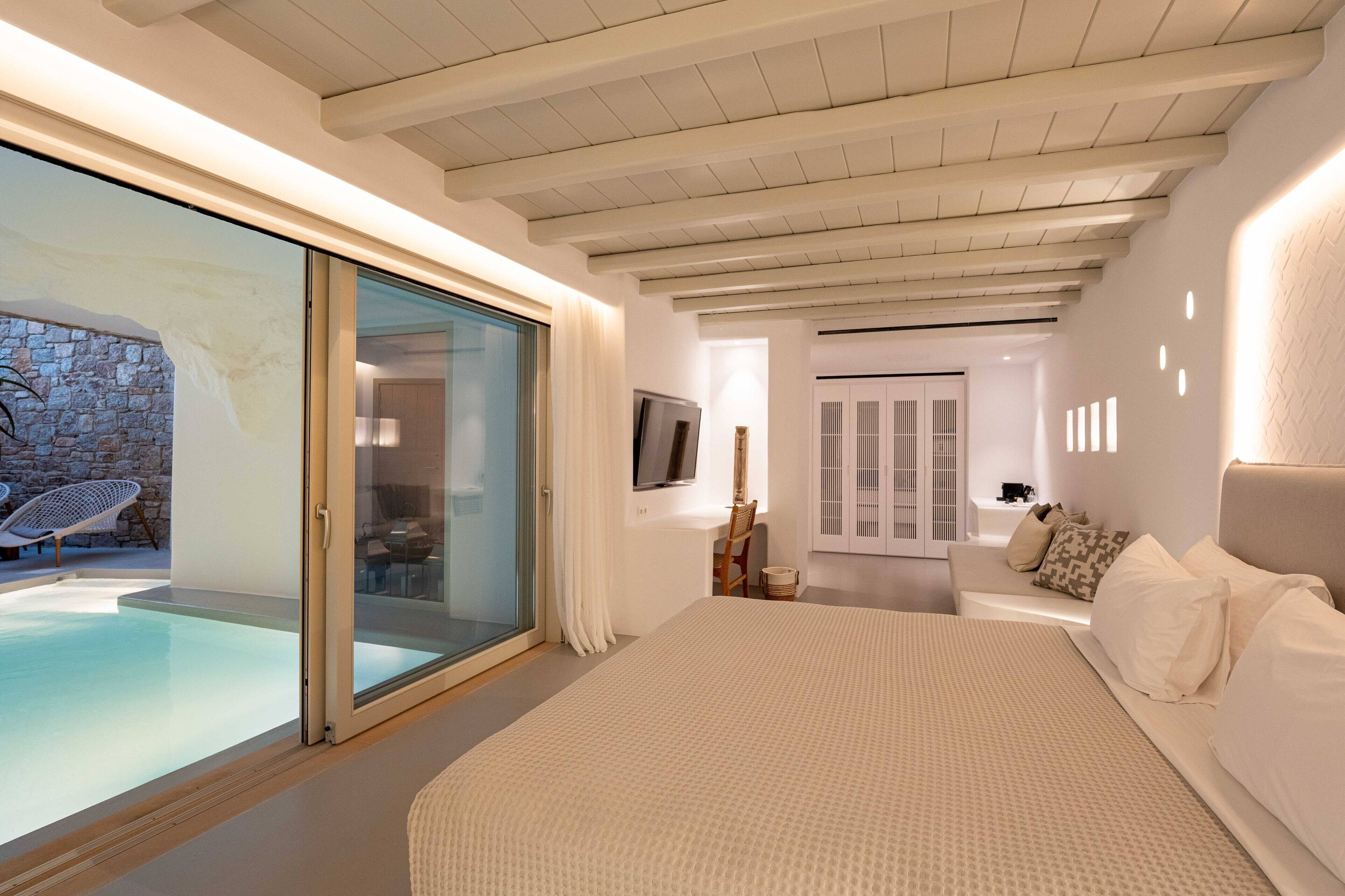 Un dormitorio moderno con una cama grande, un ventanal de vidrio que da a una zona de piscina y un rincón de descanso acogedor con chimenea.