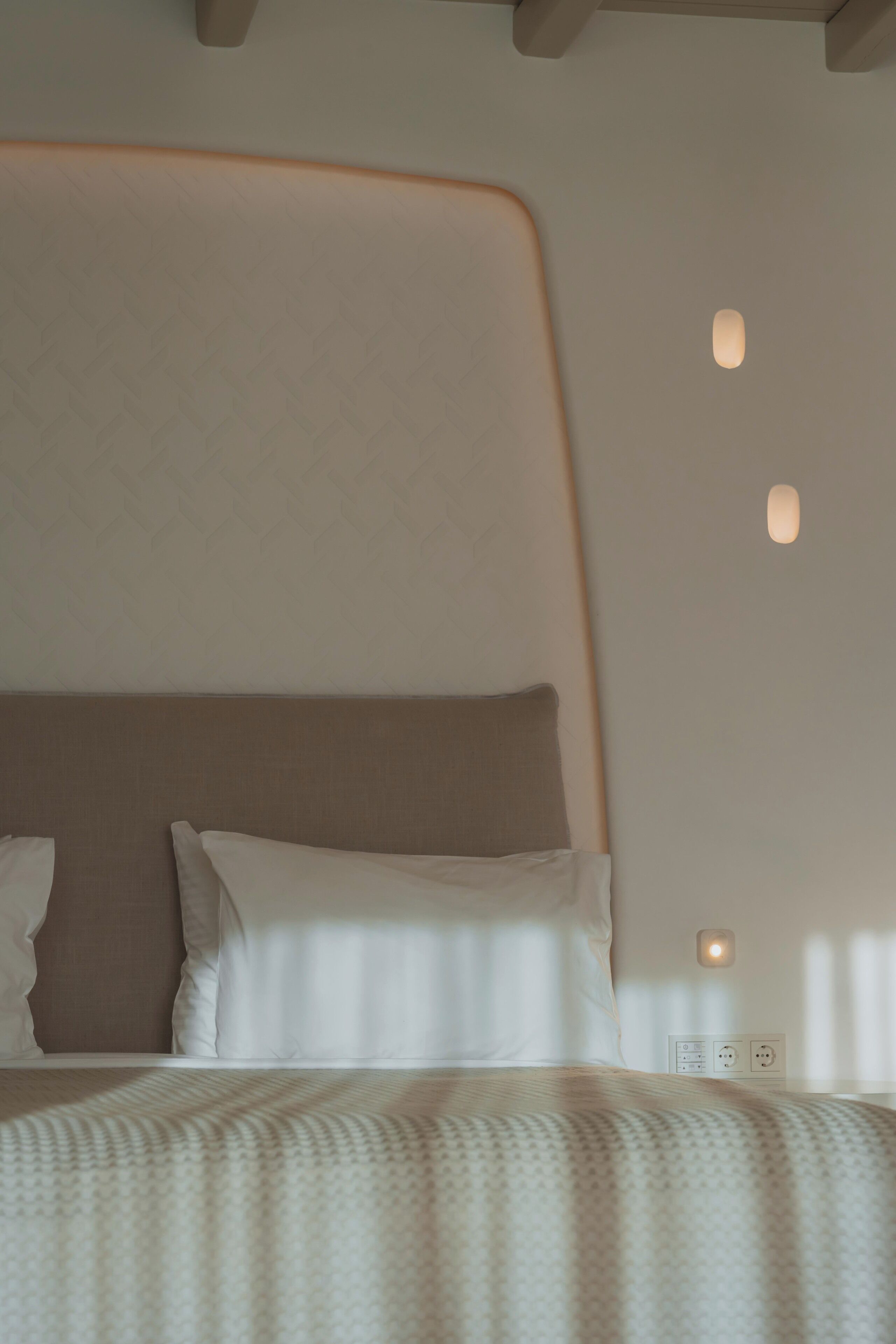 A modern bedroom with a large bed, a headboard, and a wall-mounted light fixture.