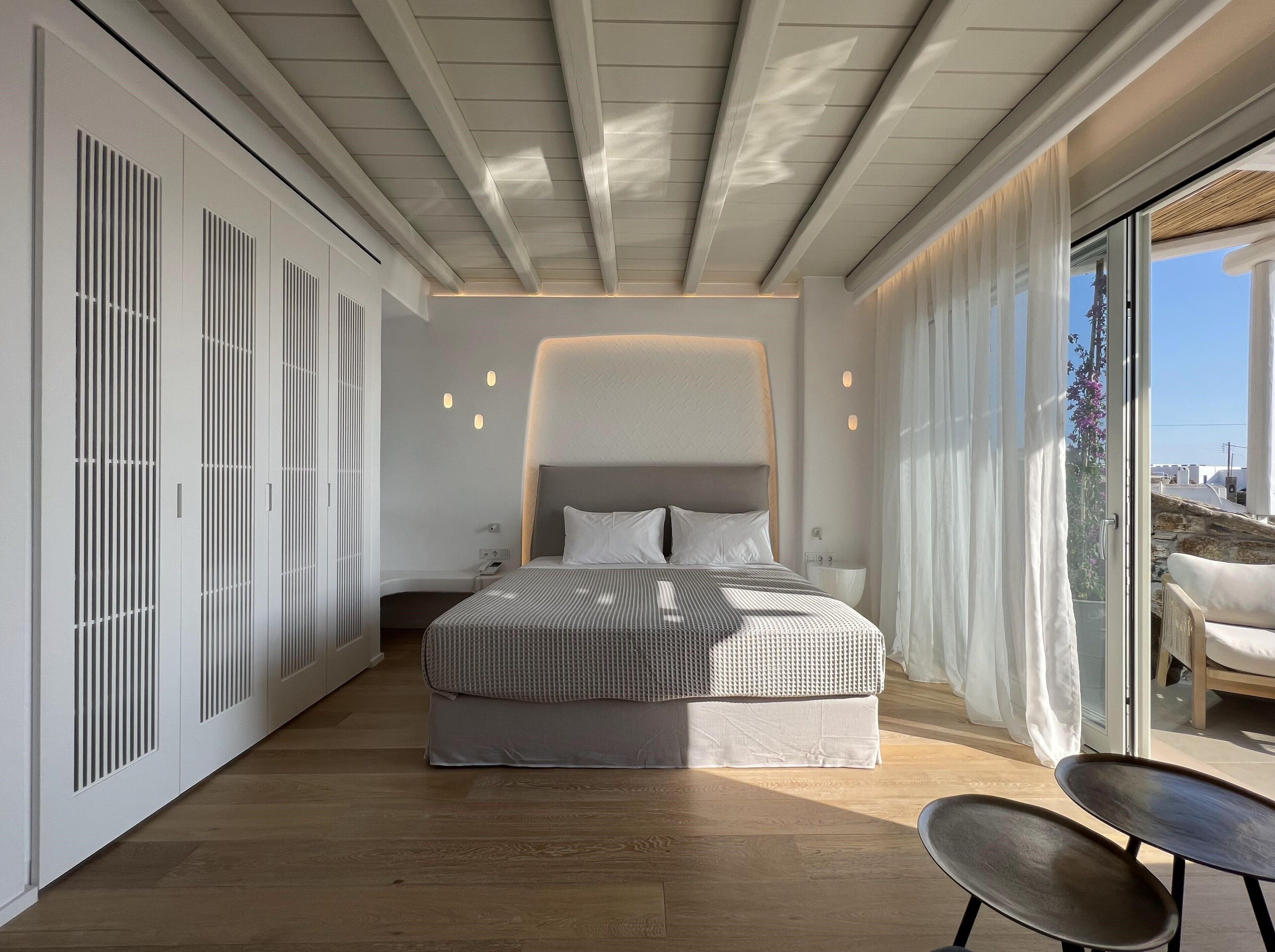 Une chambre moderne avec un grand lit, une porte-fenêtre coulissante donnant sur un balcon et un plancher en bois.