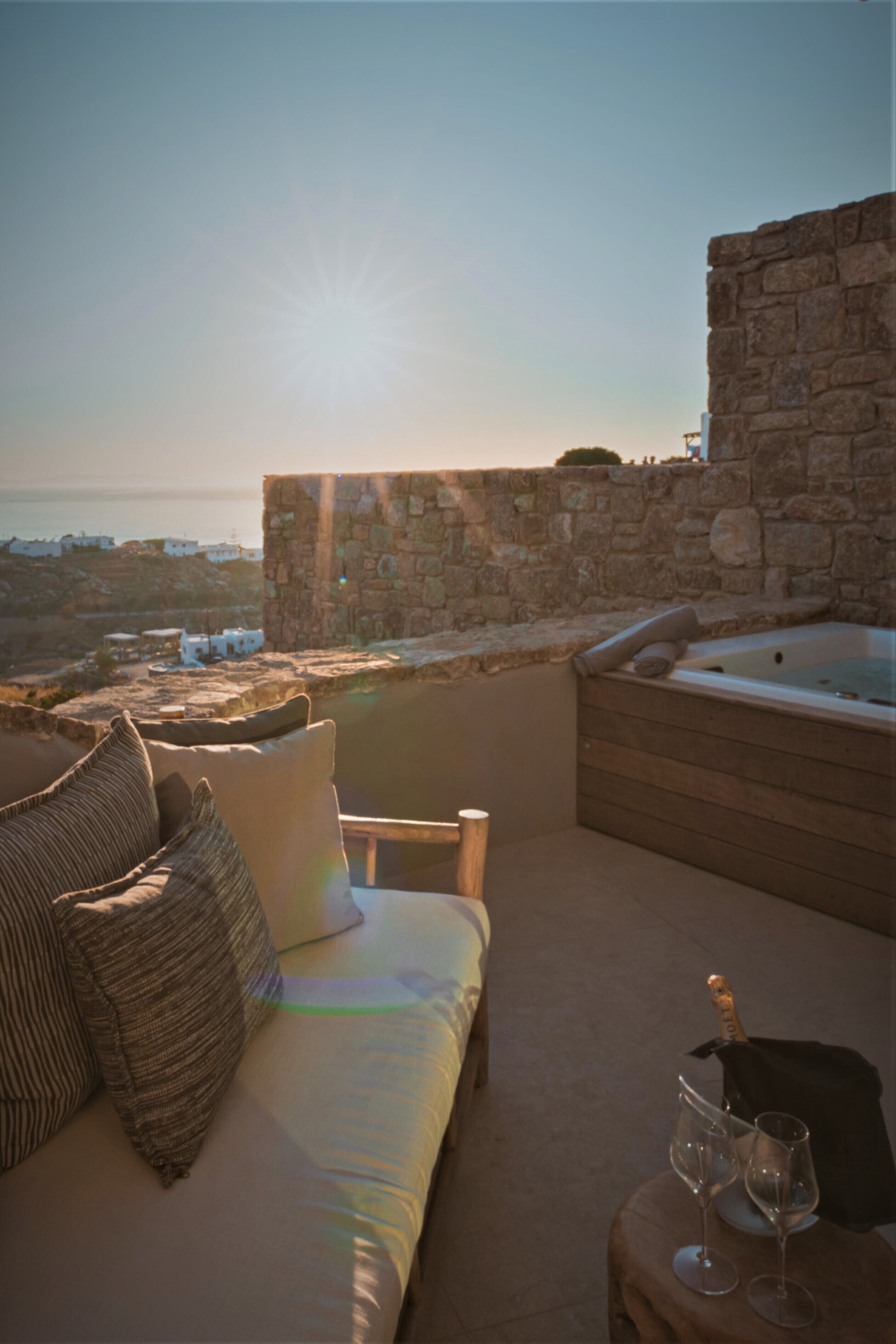 Un espacio al aire libre con sol, con zona de estar, pared de piedra, bañera de hidromasaje y vista al mar.
