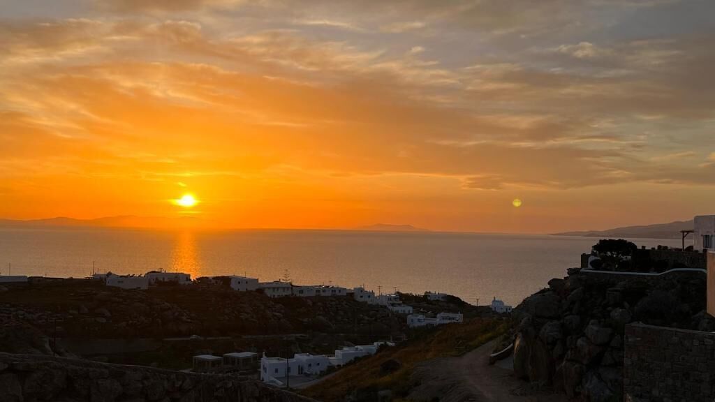 Vista de un atardecer costero con edificios blancos y un muro de piedra.