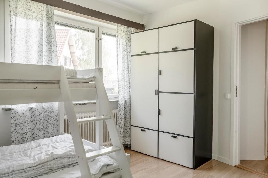 A room with a bunk bed, a wardrobe, and a window with curtains.