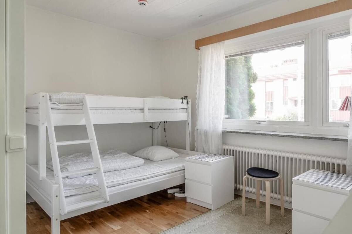 A bunk bed with a desk and chair, a radiator, and a window with curtains.
