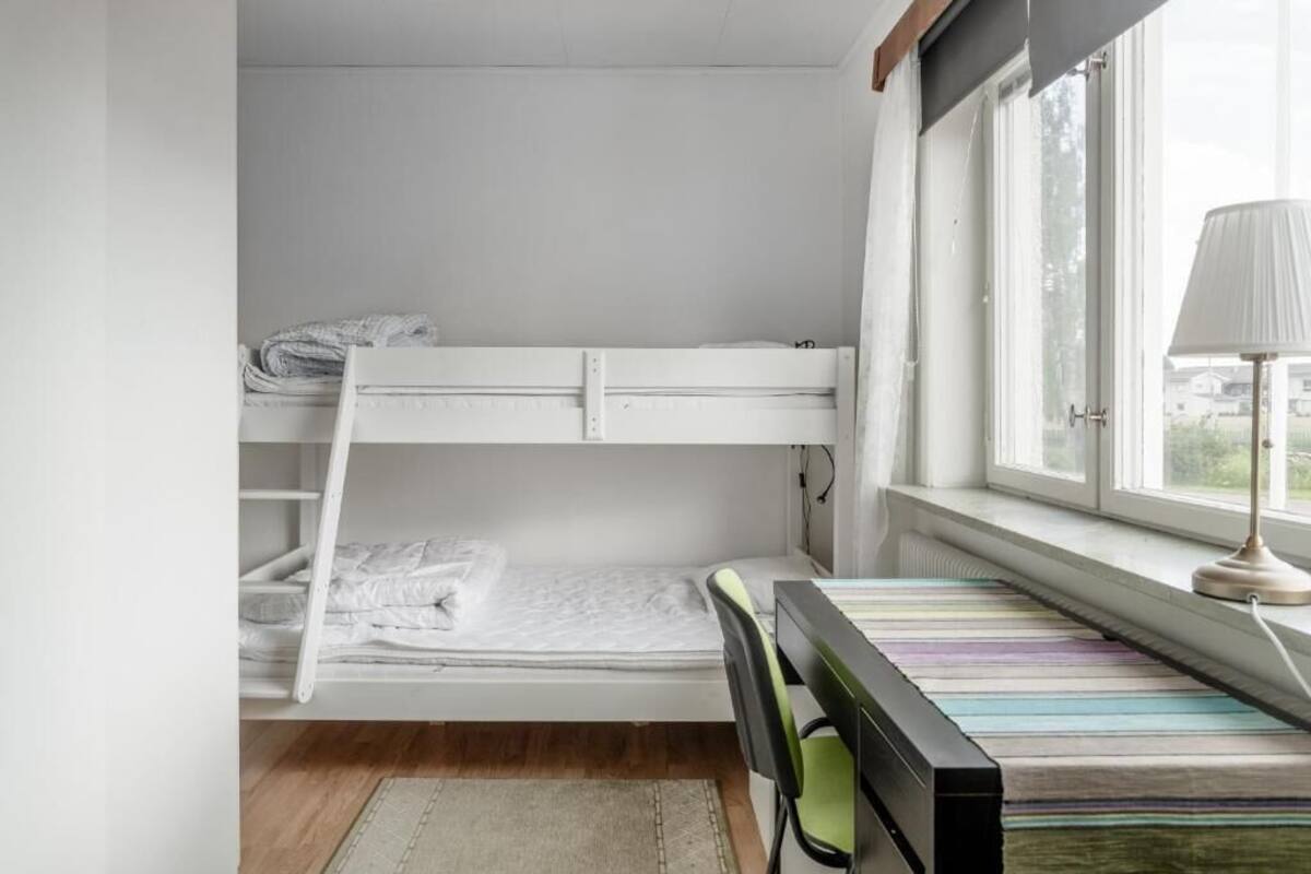A bunk bed room with a desk and chair, a window with curtains, and a lamp on the desk.