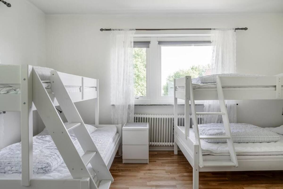 A bunk bed room with a window, white curtains, and a radiator.