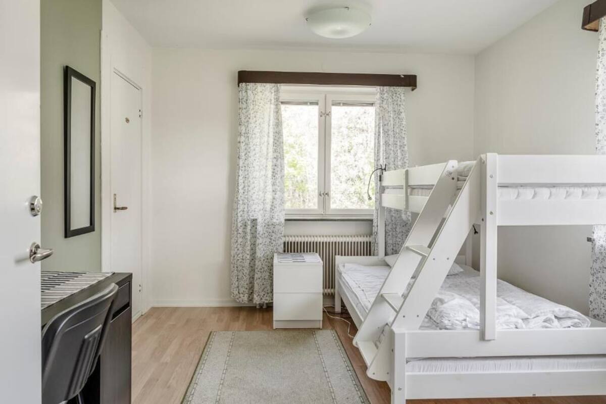 A bedroom with a bunk bed, a desk with a chair, a radiator, and a window with curtains.