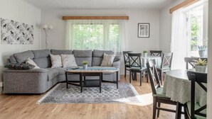 A modern living room with a grey sectional sofa, a coffee table, and a dining area with a round table and chairs. - Vandrarhemmet Stranden i Mora (Mora)