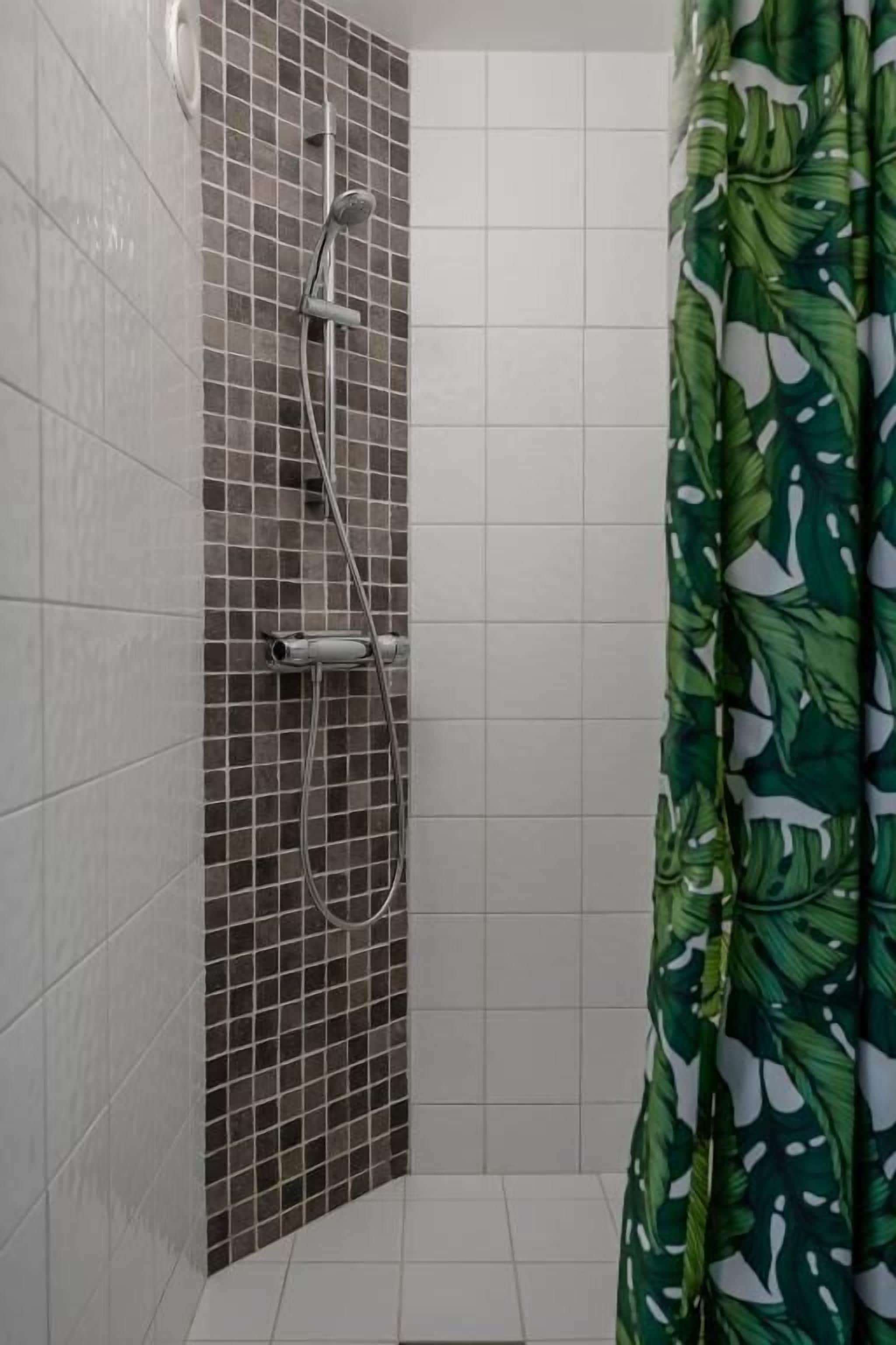 Una ducha con pared de azulejos, un cabezal de ducha y una cortina con estampado de hojas.