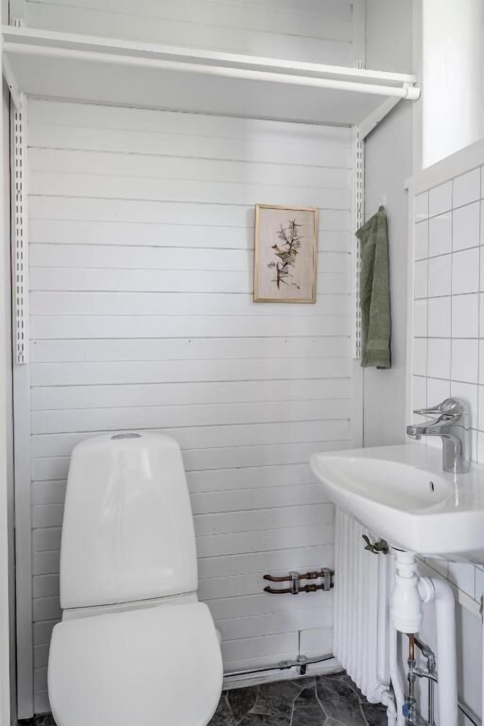 A bathroom with a toilet, a sink, a towel rack, and a framed picture on the wall.