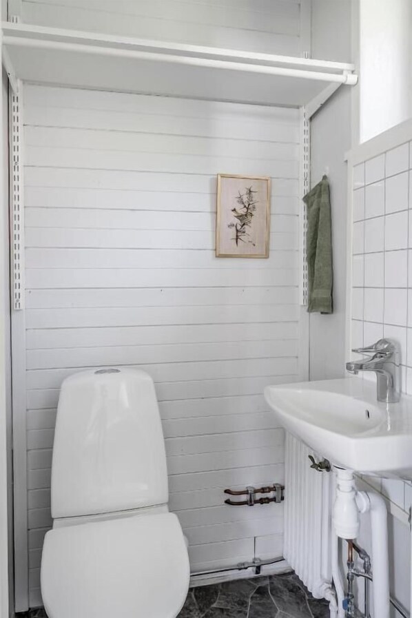 A bathroom with a toilet, a sink, a towel rack, and a framed picture on the wall. - Vandrarhemmet Stranden i Mora (Mora)