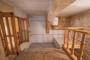 Une salle de bain avec une porte en bois, une douche, une baignoire blanche et un mur en pierre.