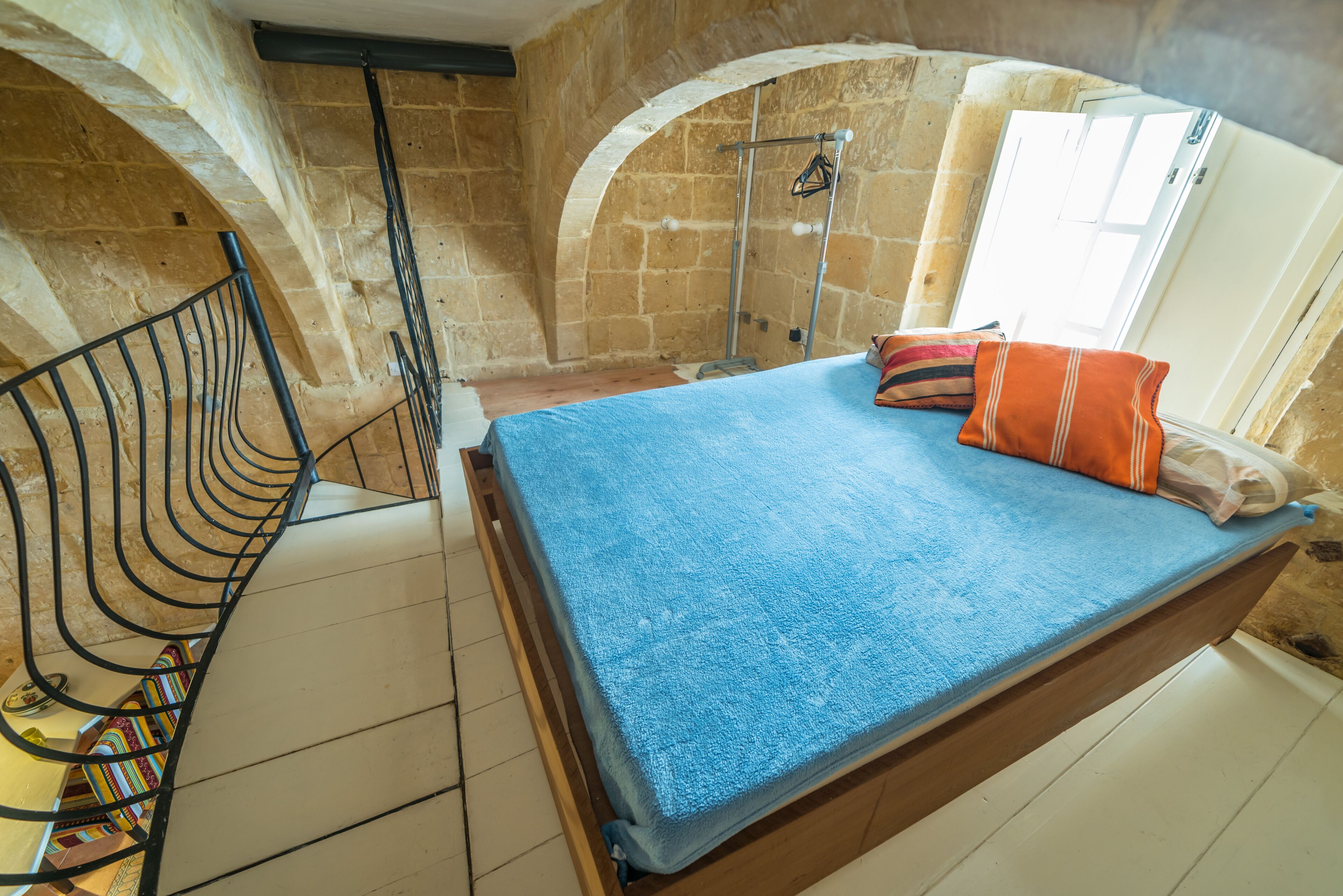 A bedroom with a wooden bed, a metal ladder, and stone walls.