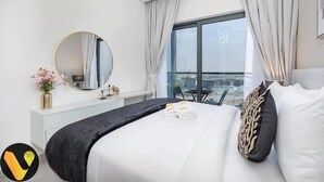 Moderni hotellihuone, jossa on suuri sänky, pyöreä peili, näkymä kaupunkiin suurista ikkunoista sekä parveke, jossa on tuoli.