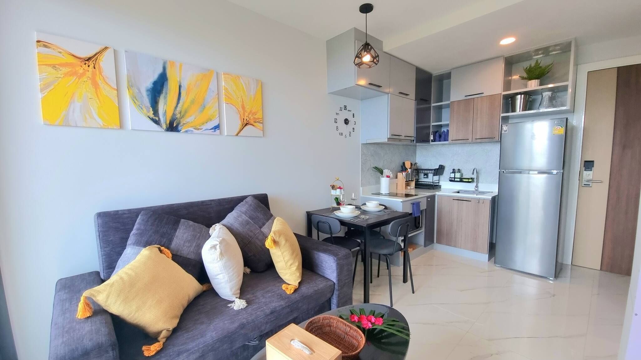 A modern apartment with a grey sofa, a dining table, and a kitchen area.