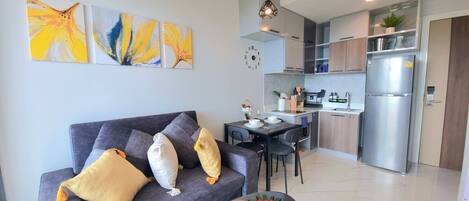 A modern apartment with a grey sofa, a dining table, and a kitchen area.