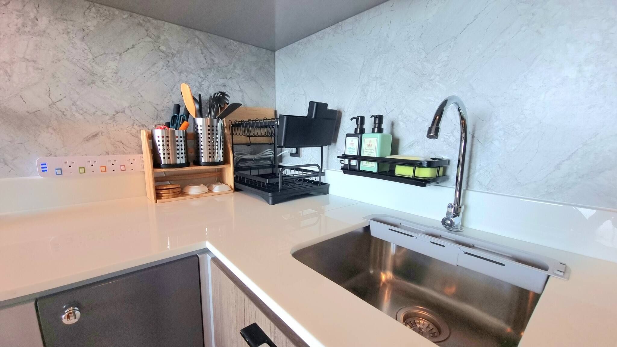 A modern kitchen with a stainless steel sink, a black coffee machine, and a wooden utensil holder.