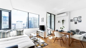 A modern, well-lit room with a large window, a bed, a dining area, and a TV.