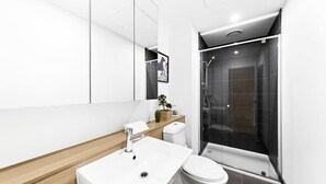 A modern bathroom with a white sink, toilet, and a glass-enclosed shower.