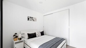 A bedroom with a bed, a nightstand, a bedside table, a wall-mounted artwork, and a closet.