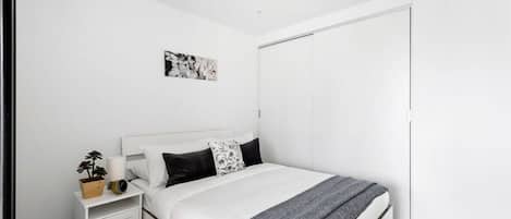 Une chambre à coucher comprenant un lit, une table de chevet, une commode, une œuvre d’art accrochée au mur et un placard.