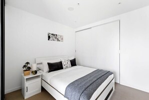 A bedroom with a bed, a nightstand, a bedside table, a wall-mounted artwork, and a closet. - Spacious Southern Cross Stay, Cozy & Central Home (Melbourne)