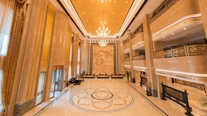 Um hall amplo com um lustre imponente, piso de mármore e um balcão de recepção.