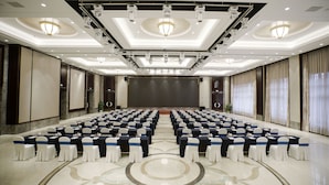 Uma sala de conferência com fileiras de mesas e cadeiras, um palco e um candelabro.